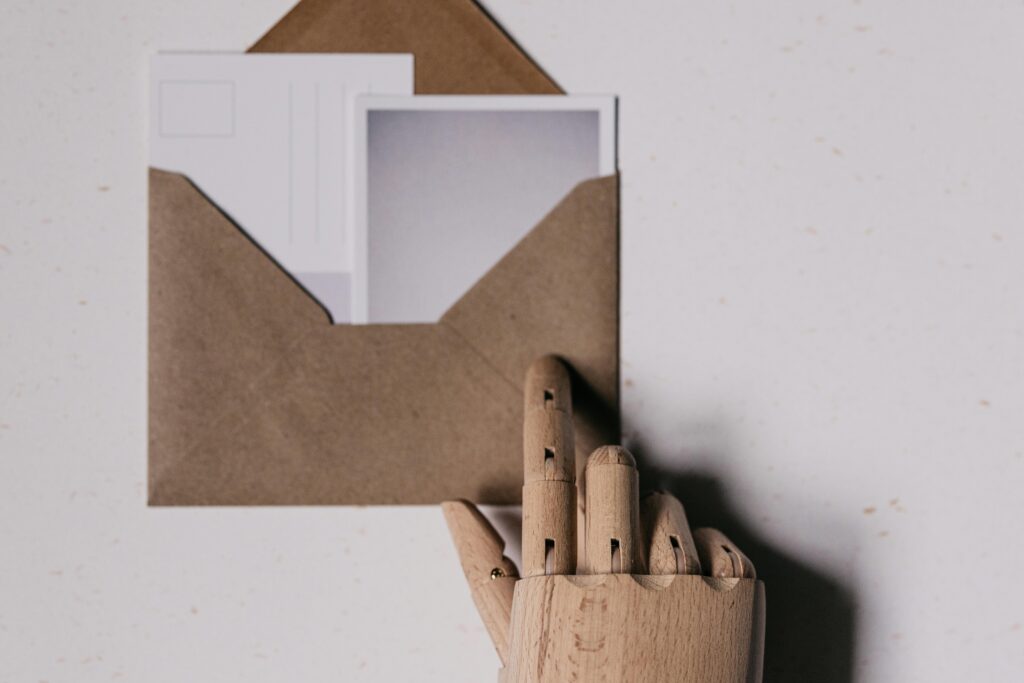 A wooden mannequin hand holds a brown envelope containing blank postcards.