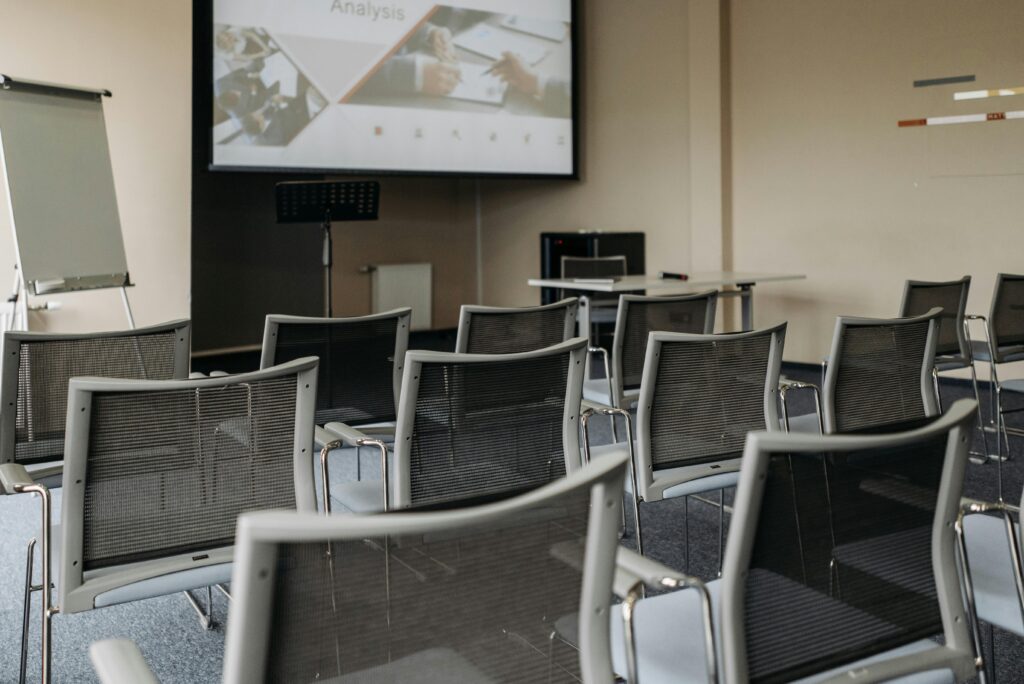 Modern conference room setup with empty chairs, projector screen, and presentation equipment.