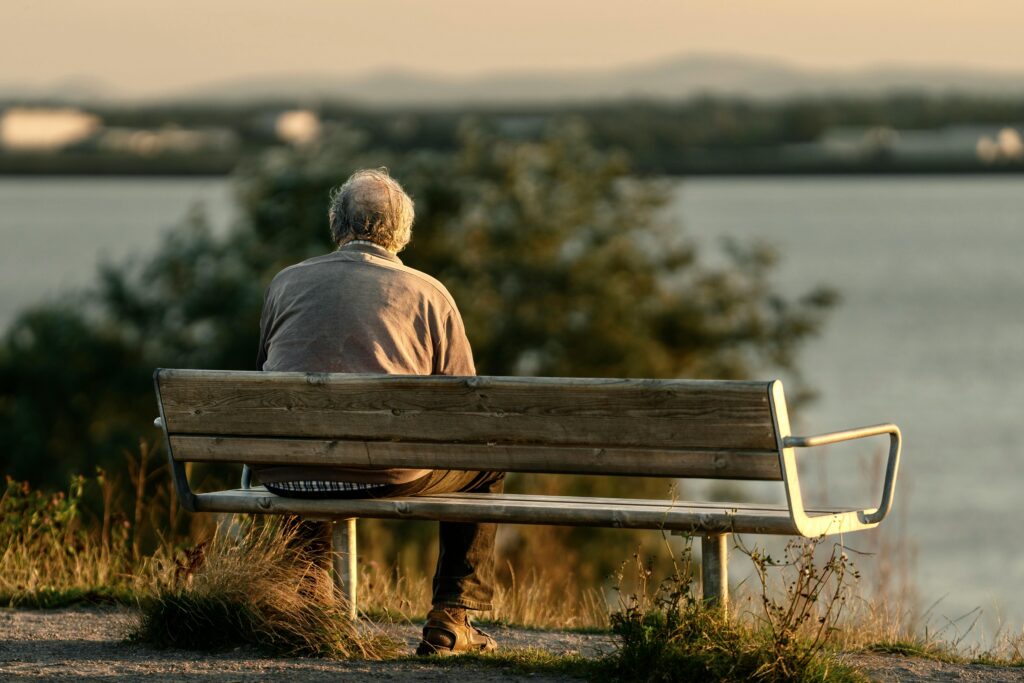 Rentenreform: Änderungen und Vertrauensschutz Serene scene of a senior man sitting on a bench by a lake during sunset.
