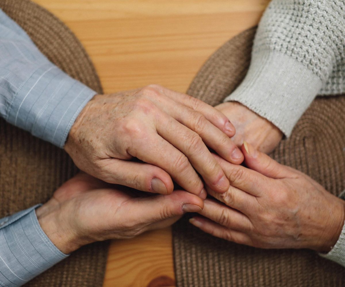 Close-up of elderly hands holding on a wooden table, symbolizing love and connection.